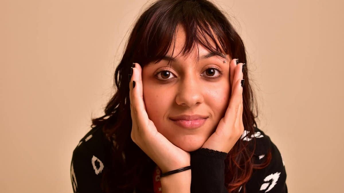 Close-up of a young woman with hands on face, gazing serenely indoors.