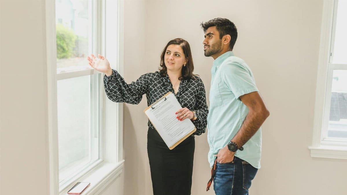 A real estate agent discusses property details with a client indoors, highlighting the view through large windows.