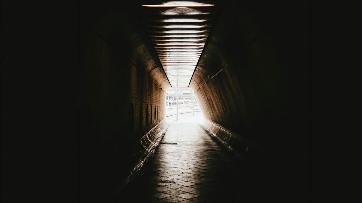 A dark and mysterious tunnel leading to a brightly lit street, creating a dramatic contrast.