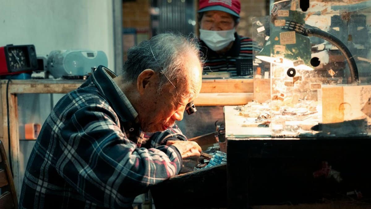 An elderly watchmaker meticulously repairs a watch in a dimly lit workshop, symbolizing dedication to craft.