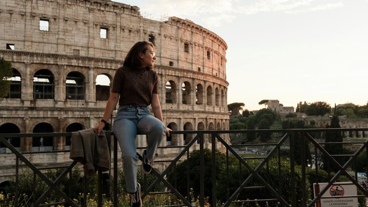 Woman sitting by the Colosseum in Rome, enjoying a sunny day with lush greenery.