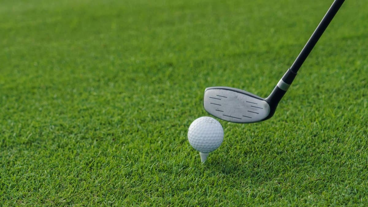 Golf club poised to hit a golf ball on a tee, set against a lush green grass background.