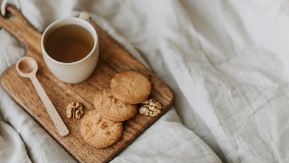 A warm mug of tea with cookies and walnuts on a wooden board, perfect for a cozy snack.