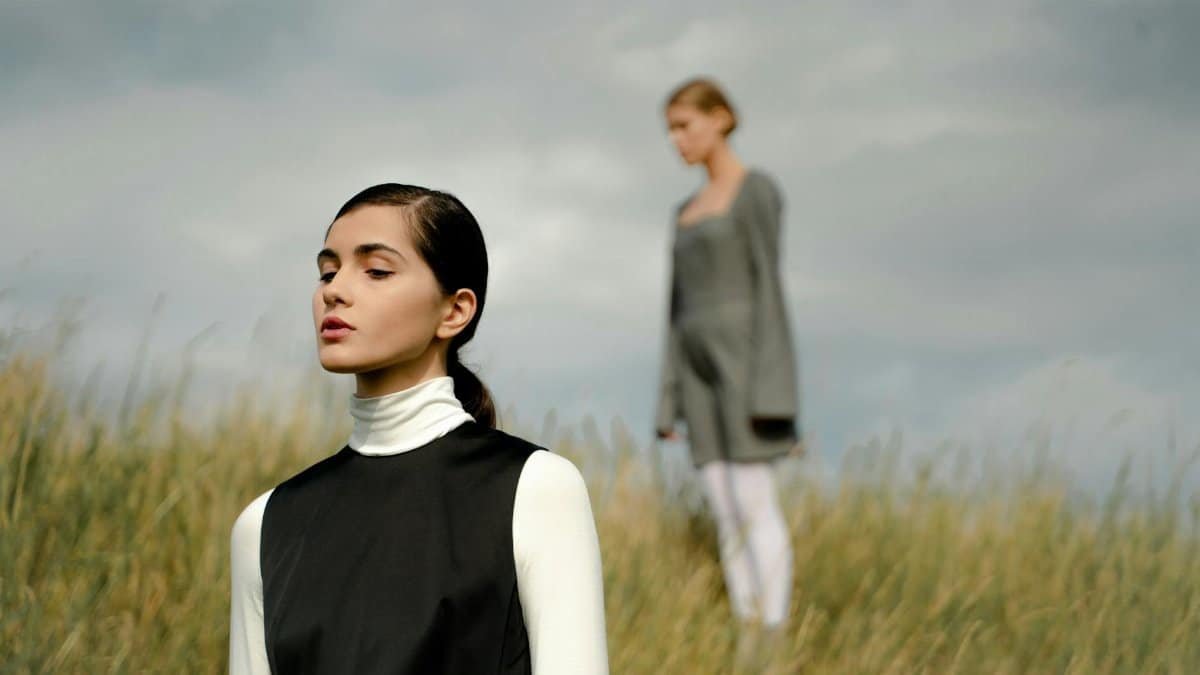 Two women standing in a peaceful grass field, contemplating the serene surroundings on a cloudy day.