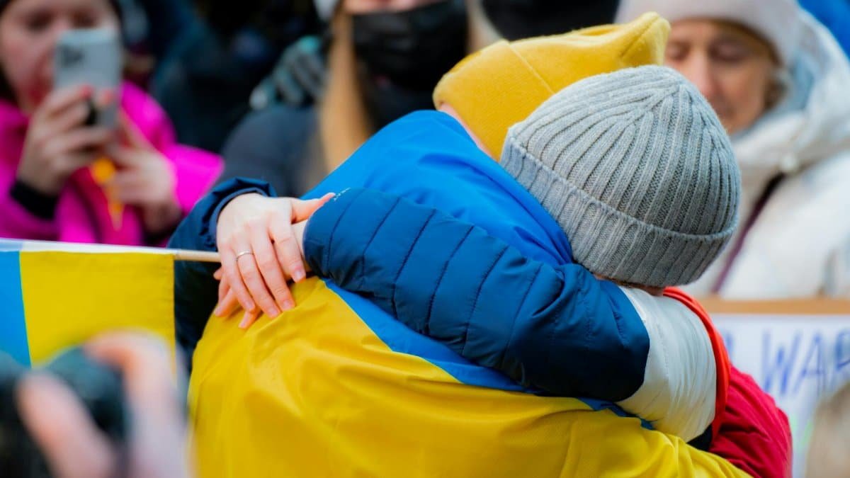 Close-up of two adults embracing at a New York protest, with people in background.