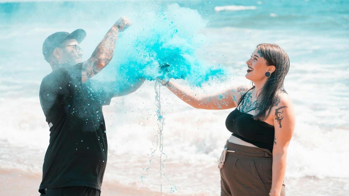 Happy couple celebrates gender reveal with blue powder on Santa Monica beach.