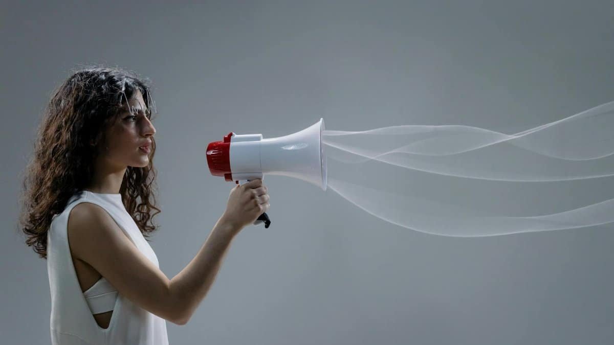 Woman using a megaphone emitting sound waves on a gray background.