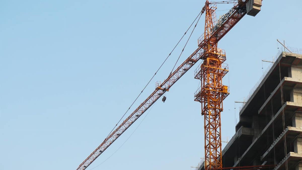 Low angle view of a tower crane beside a building under construction against a blue sky.