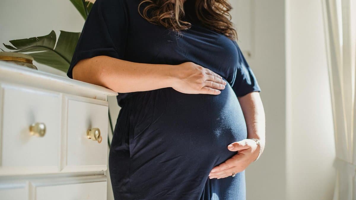 A serene image of a pregnant woman standing indoors, embracing motherhood with calmness and anticipation.