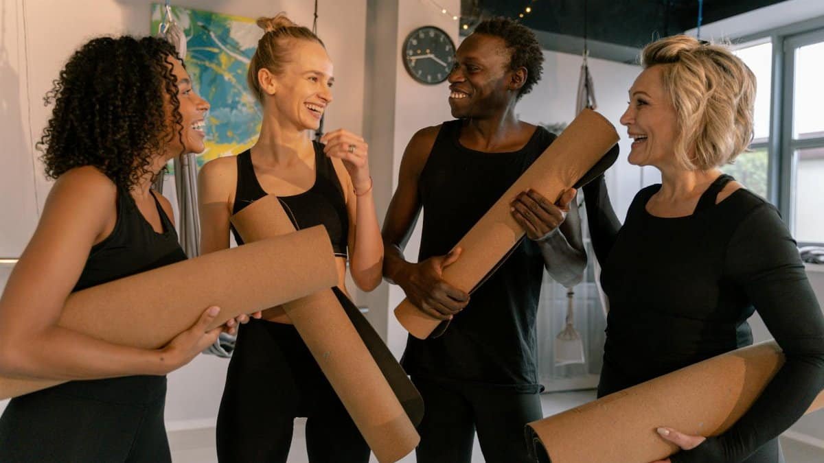 Group of smiling adults holding yoga mats, embracing fitness and wellness indoors.
