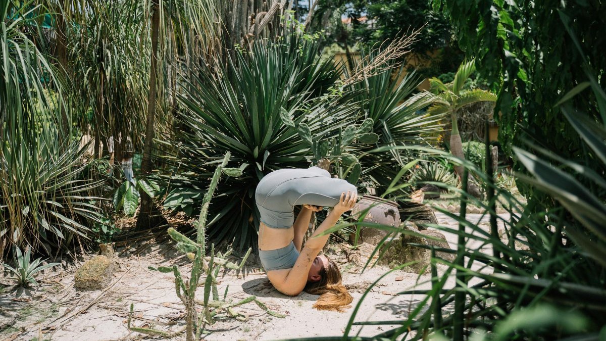 A woman performing a headstand yoga pose outdoors in a vibrant, lush garden setting.