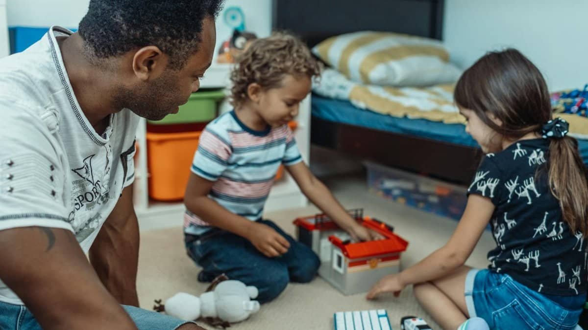 A father and two children enjoying playtime together in a cozy bedroom setting.