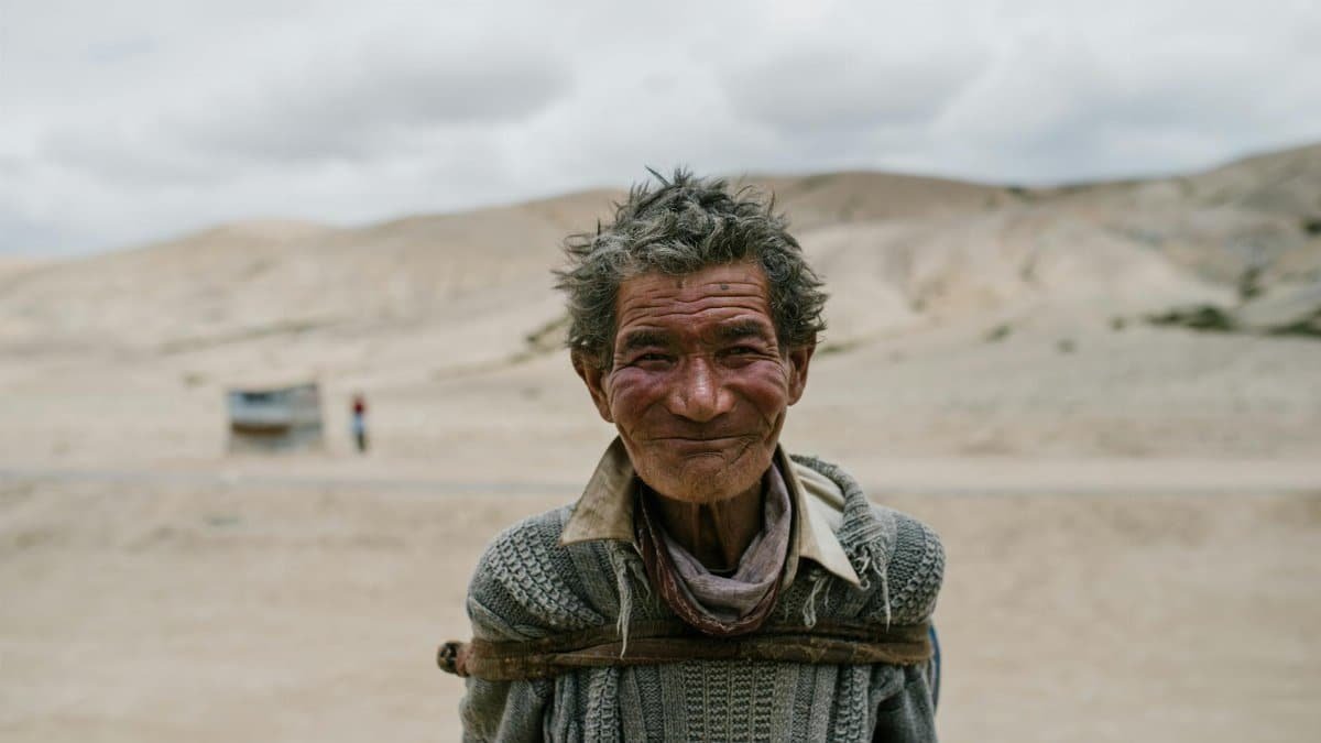 Portrait of a smiling elderly man standing in a desert landscape, exuding warmth and resilience.