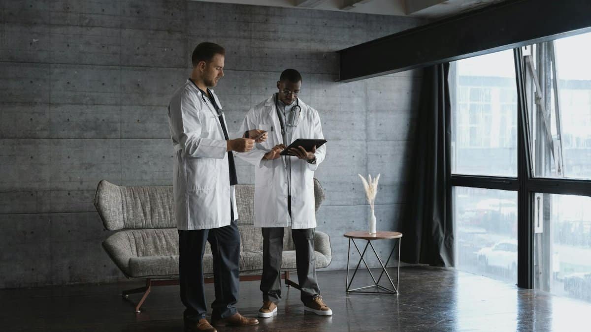 Two doctors in an industrial office discuss patient data on a digital tablet.