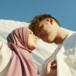 A couple looks at each other lovingly under a bright blue sky, embracing togetherness.