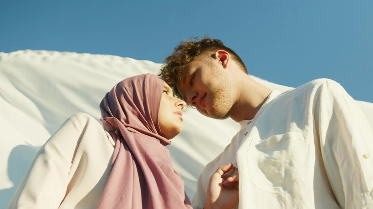 A couple looks at each other lovingly under a bright blue sky, embracing togetherness.