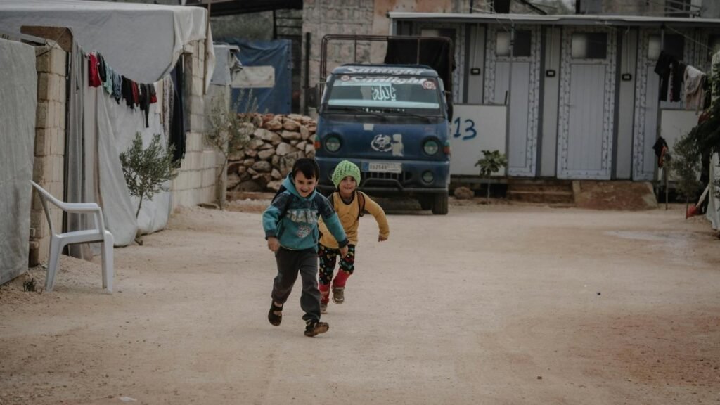 Two children joyfully running down a street in Idlib, capturing a moment of fun and energy.