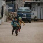 Two children joyfully running down a street in Idlib, capturing a moment of fun and energy.