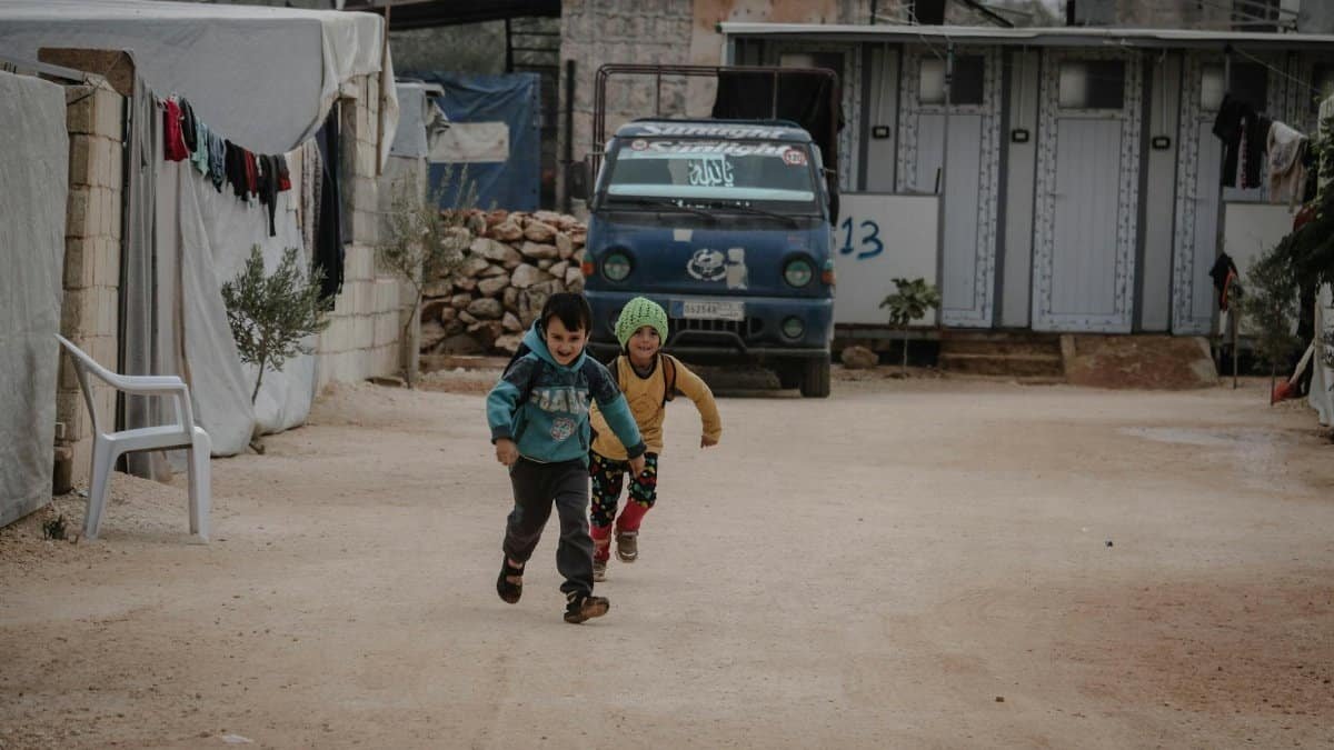 Two children joyfully running down a street in Idlib, capturing a moment of fun and energy.