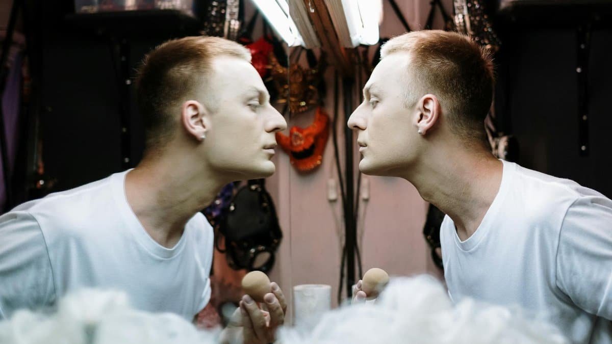 Drag performer applying makeup in a dressing room mirror before a show.