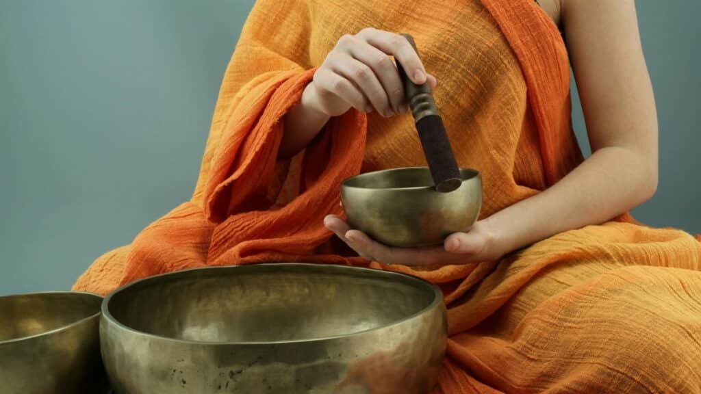 Person in traditional attire using Tibetan singing bowls in a meditative practice.