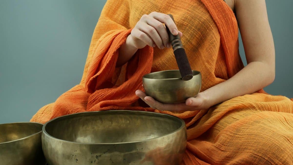 Person in traditional attire using Tibetan singing bowls in a meditative practice.