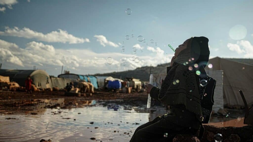 A woman in a hijab joyfully blows bubbles in a refugee camp in Idlib, Syria.