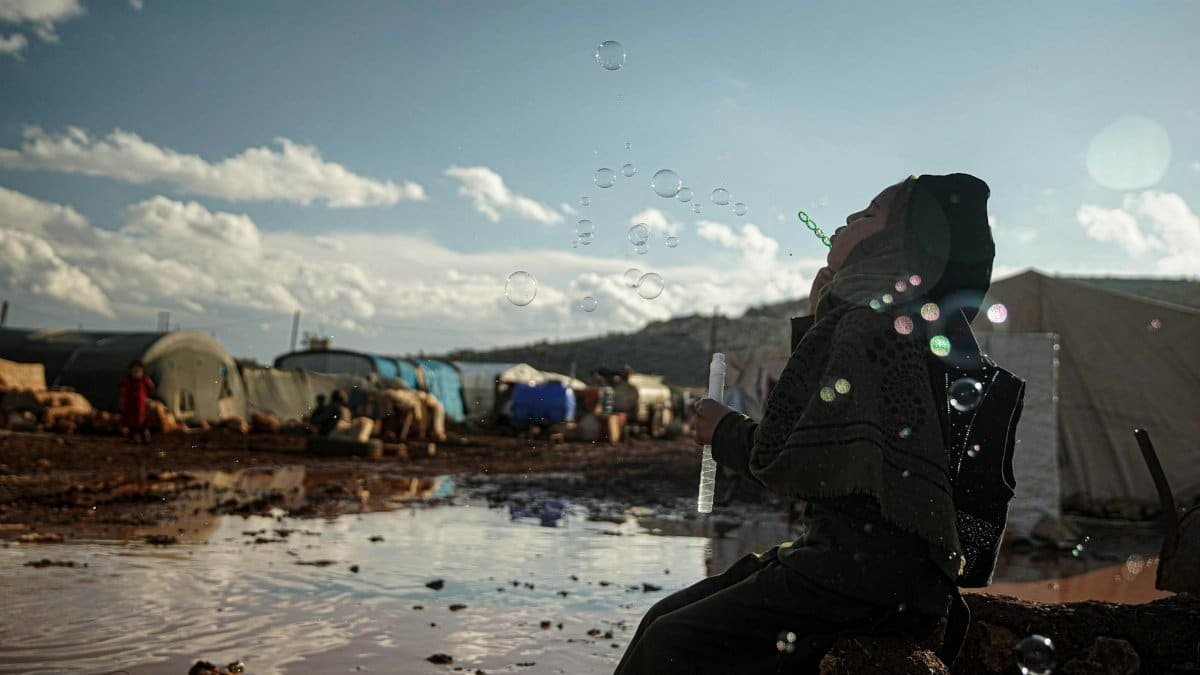 A woman in a hijab joyfully blows bubbles in a refugee camp in Idlib, Syria.