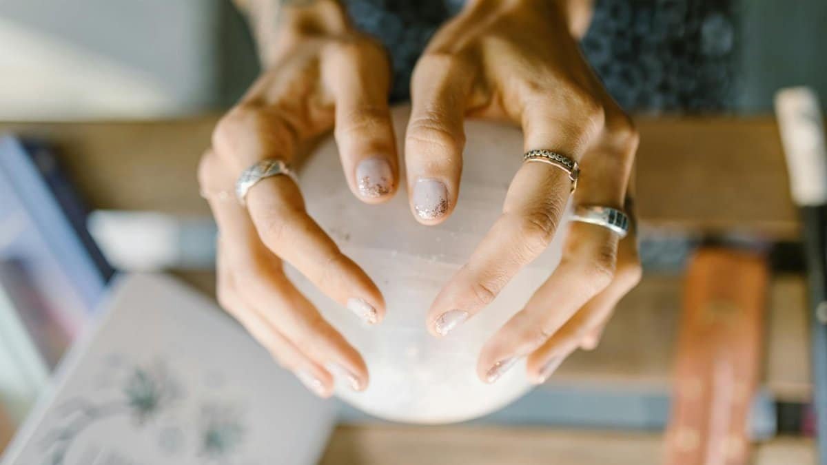 Hands wearing rings holding a crystal sphere, symbolizing spirituality and healing.