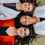 Three smiling women lying on the floor wearing vibrant clothing, symbolizing joy and friendship.