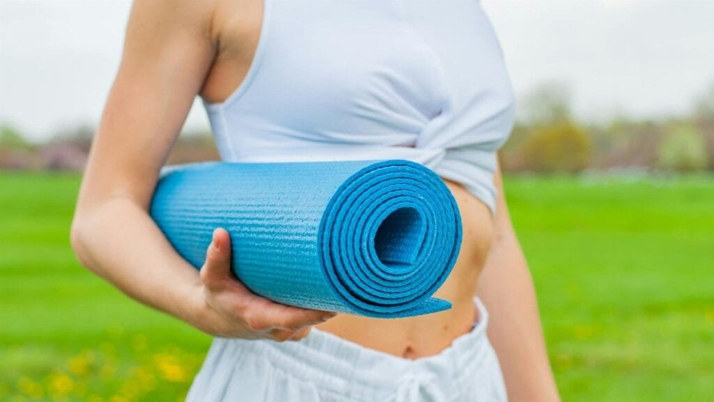 Close-up of a woman holding a blue yoga mat in a green outdoor setting during spring.