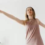 From below of calm young female performing Warrior II yoga asana with extended arms and closed eyes