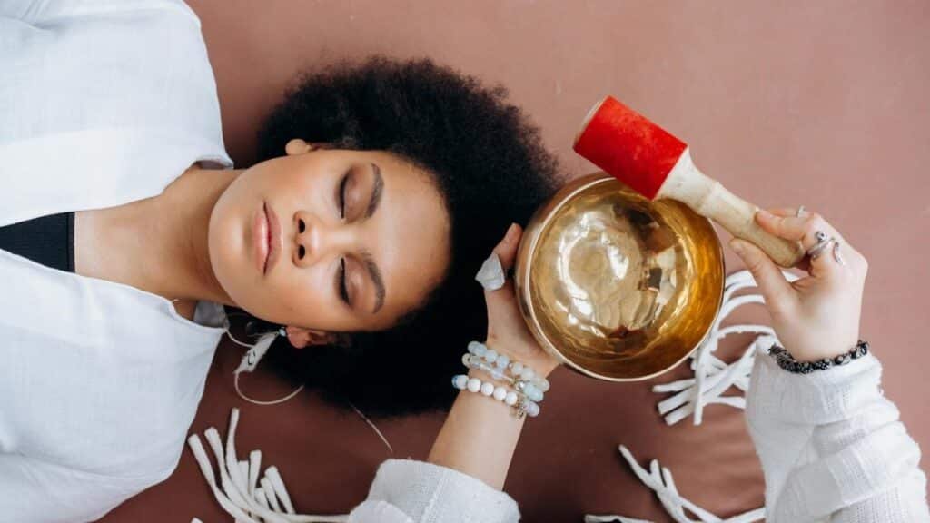 A woman experiencing sound healing therapy with a Tibetan singing bowl indoors