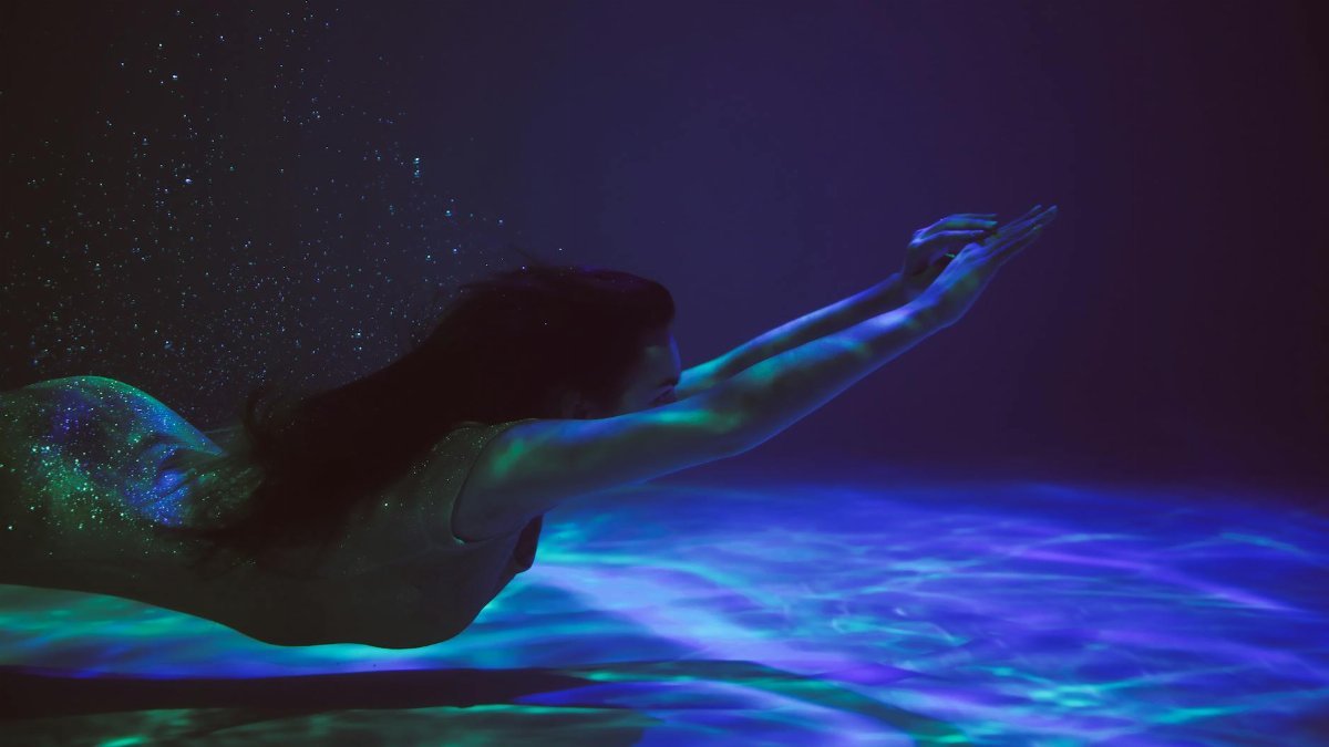 A serene woman swimming underwater, surrounded by ethereal light and bubbles.