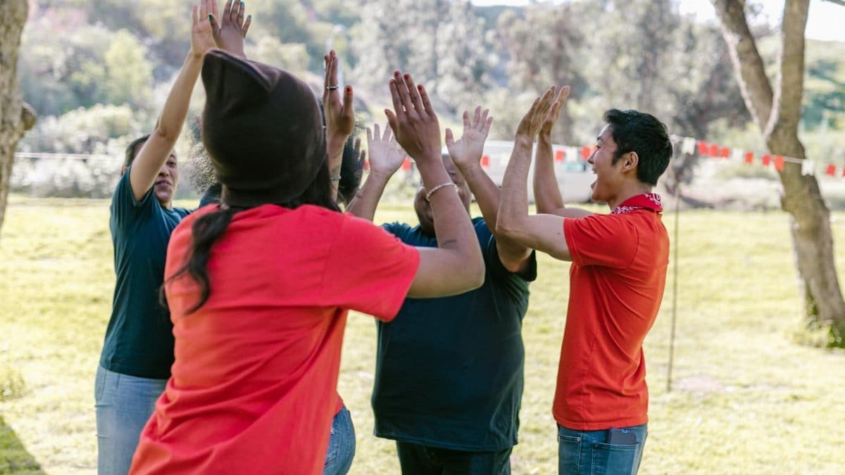 Diverse friends in park high-fiving during fun team-building exercise.