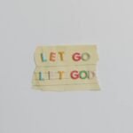 Minimalist image of a torn paper with the phrase 'Let Go, Let God' in colorful letters.