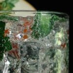 Close-up of a glass with sparkling water, ice, mint leaves, and fruit slice.