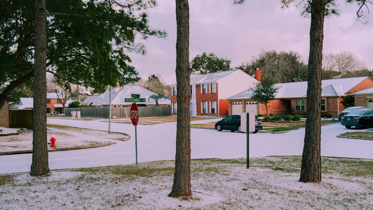 A serene suburban street covered in snow, featuring houses and trees on a winter day.