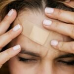 A person with a band aid on their forehead holds their head in pain, eyes closed.