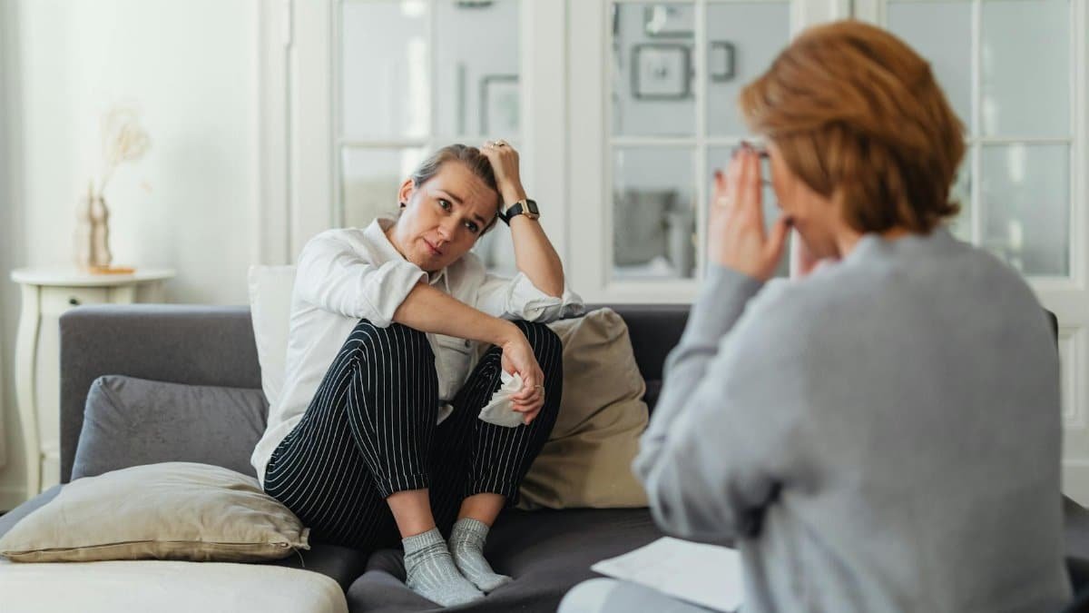 A woman sits on a couch during a therapy session, talking to a therapist.