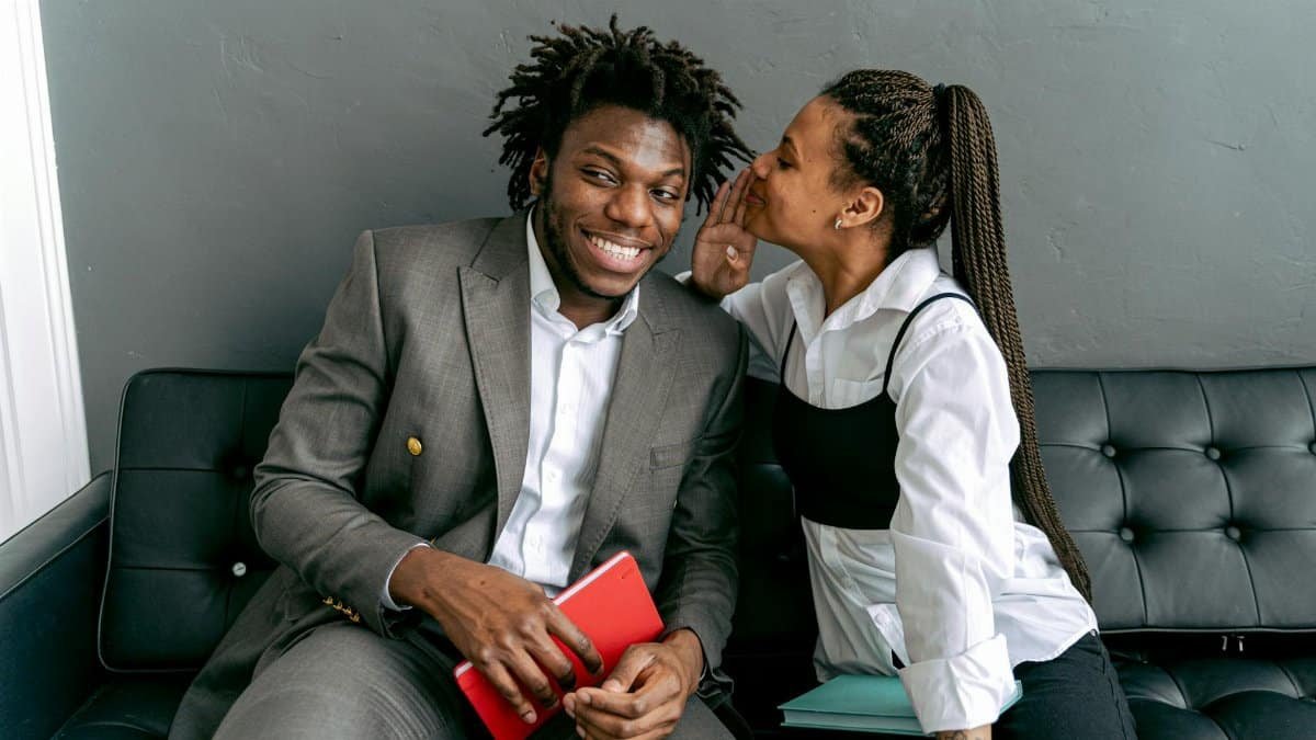 Two professionals sharing a secret on a modern black couch, indoors.