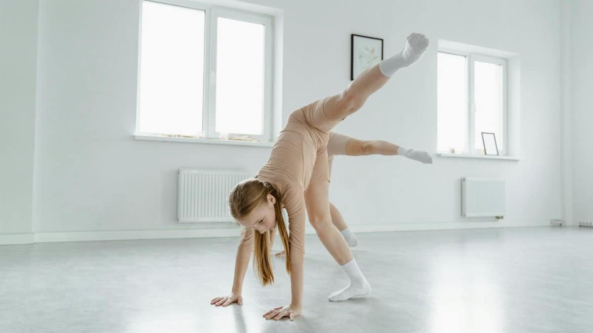 A young female dancer in a bright studio performing a graceful handstand pose.