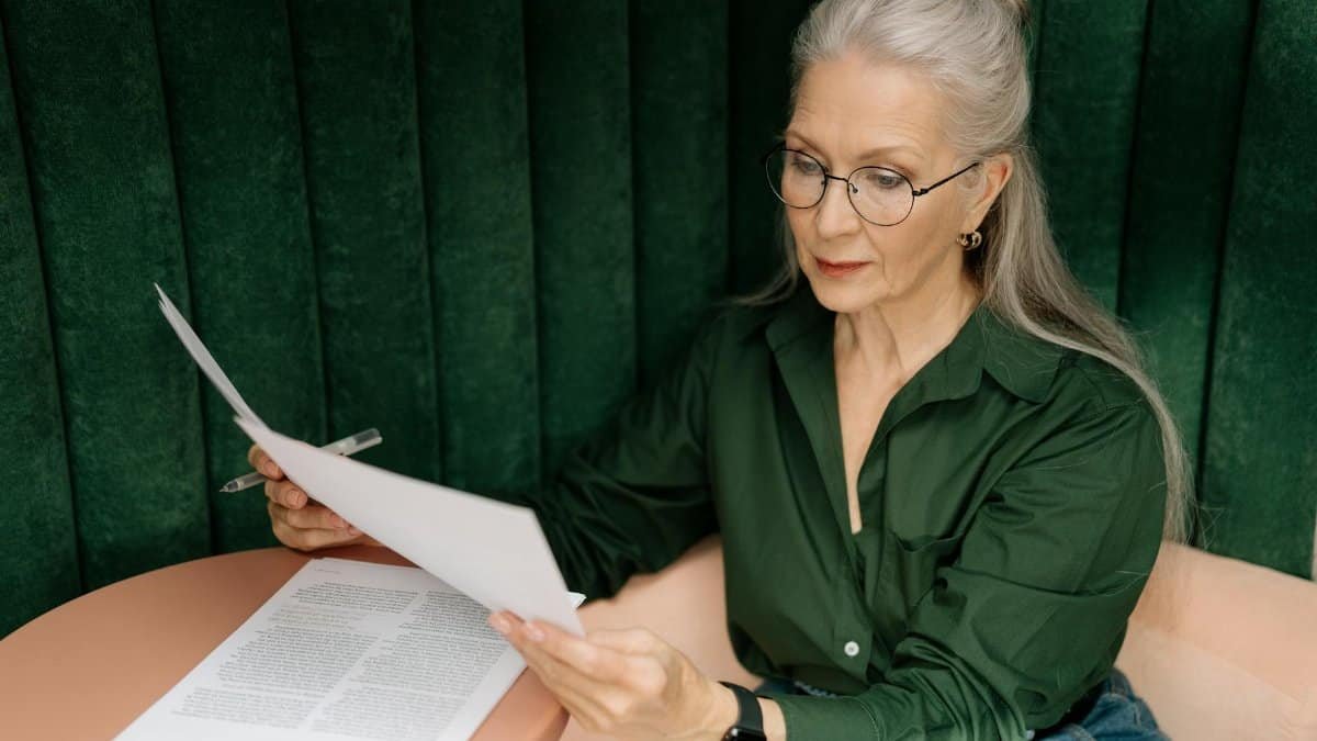 Senior woman wearing glasses, reading documents at a desk indoors, showcasing professional focus.