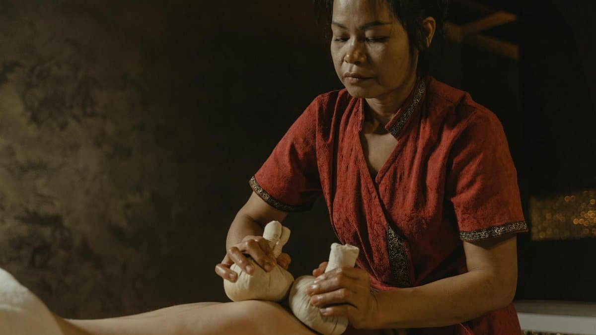 A masseuse performing therapeutic massage using herbal compress on a client for relaxation.