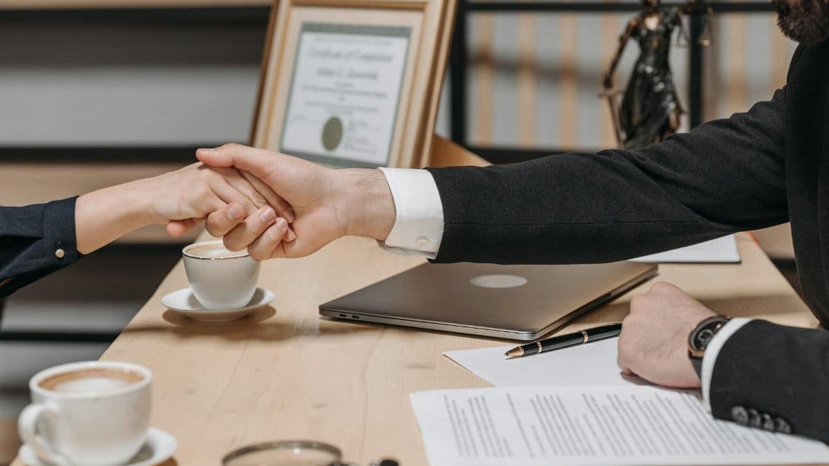 A formal handshake over a business contract in a corporate office setting.