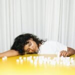 A woman leans on a yellow table surrounded by sugar cubes, highlighting a concept of fatigue and health awareness.
