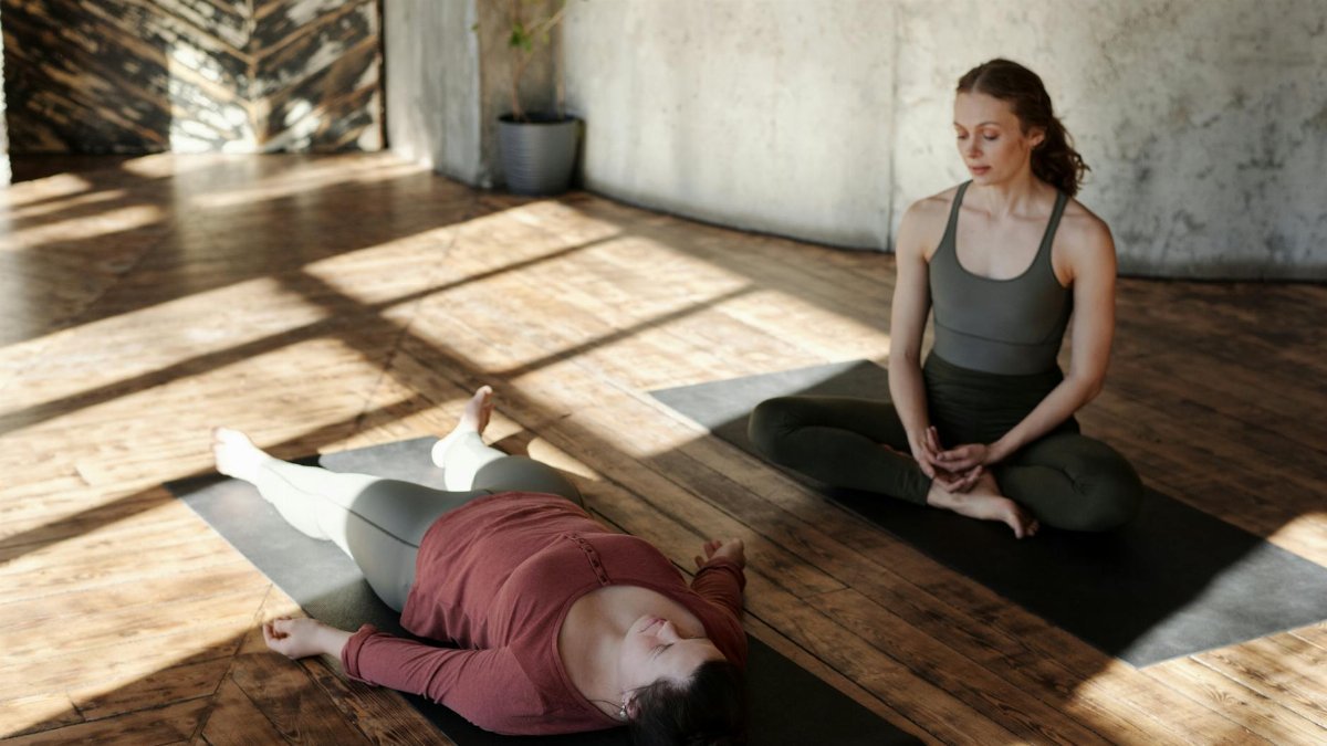 Two women practicing yoga indoors with sunlight streaming in, highlighting focus and relaxation.
