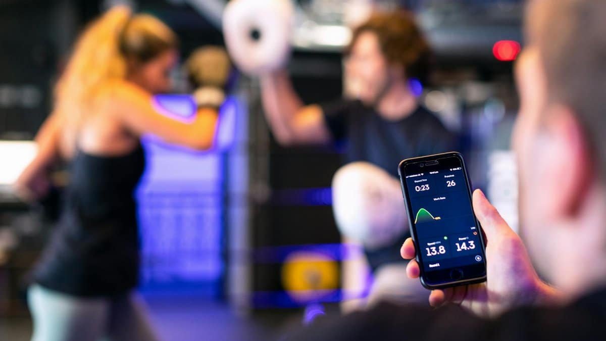 A woman boxing with a trainer while a fitness app tracks performance on a smartphone.