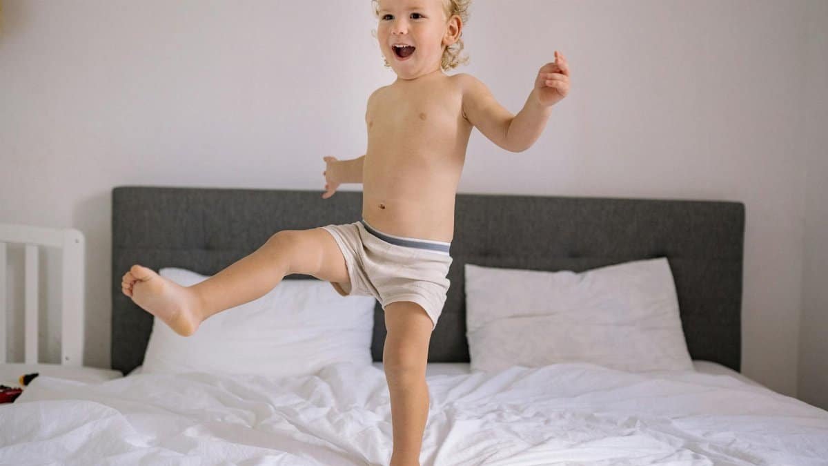 A cheerful child enjoying a playful moment jumping on a bed in a cozy bedroom setting.