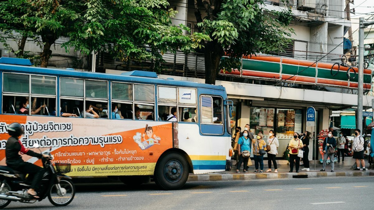 A crowded street scene in Thailand with a bus and pedestrians waiting. Urban life captured.